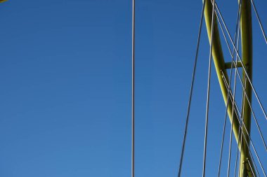 Canlı, mavi gökyüzüne karşı modern bir köprü yapısının minimalist yakın çekimi. Görüntü, köprü kablolarının ve çelik elementlerin yapısal detaylarını vurguluyor.