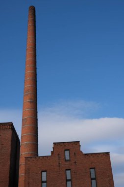 Uzun kırmızı tuğlalı sanayi bacası açık mavi gökyüzüne doğru uzanarak sanayi ve tarih temalarını anımsatıyor. Bacanın tabanındaki bina kırmızı tuğlalarla eşleşiyor. Bu da eski bir tuğlayı işaret ediyor.