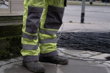 Yansıtıcı bantlı yüksek görüş mesafesi olan bir inşaat işçisinin pantolonu ve botlarının detaylı bir fotoğrafı. İş güvenliği, inşaat alanları, altyapı ve iş güvenliği ile ilgili içerik için ideal