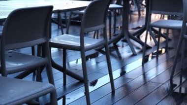 Islak masa ve sandalyelerden açık bir kafedeki dekoratif çimenlere yumuşak bir video geçişi. Işıldayan yağmurlu yüzeyler yumuşak ışığı yansıtarak kasvetli ama huzurlu bir atmosfer yaratıyor. İdeal