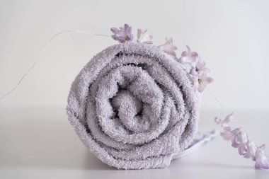 Düzgünce sarılmış lavanta renkli bir havlu narin sümbül çiçekleriyle süslenir ve yumuşak ve lüks bir estetik yaratır. Yüksek anahtarlı ışıklandırma ve temiz arkaplan havlunun dokusunu vurgular