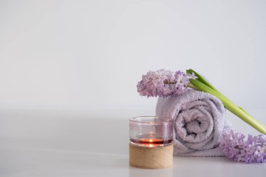Yumuşak bir lavanta havlusunun düzgünce sarıldığı, mor sümbül çiçekleri ve ahşap tabanlı cam mum tutacağıyla eşleştirilmiş lüks bir spa merkezi. Mumların sıcacık parıltısı güçlenir
