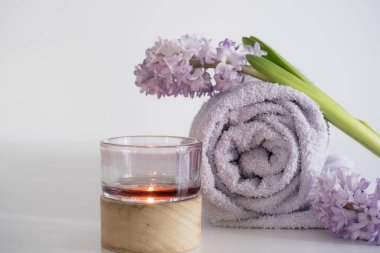 Yumuşak bir lavanta havlusu. Taze sümbül çiçekleri ve ahşap bir kabın içinde yanan bir mum. Sahne rahatlama ve kendine özen gösteriyor, spa tedavileri ve ev sağlığı kavramları için mükemmel.