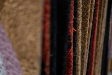 Üst üste dizilmiş paspasların detaylı bir yakın çekimi kahverengi, kırmızı, siyah ve mor lifler de dahil olmak üzere çeşitli doku ve renkleri sergiliyor. Bu resim coir ve sentetiğin karmaşık yapısını vurgular