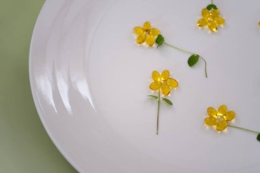 Bir bardak limonla doldurulmuş su ve beyaz bir tabakta pastel pembe arka plana yerleştirilmiş altın D vitamini içeren ferahlatıcı bir yaşam kompozisyonu. Yumuşak ışıklandırma ve narin