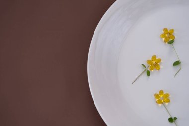 Çiğ yumurta sarısını, beyaz bir tabakta D vitamini kapsülleriyle küçük bir bardağa yerleştirilmiş kırık yumurta kabuğuna yakın plan. Pastel pembe arka plan ve yumuşak ışıklandırma hassas bir kompozisyon oluşturur.