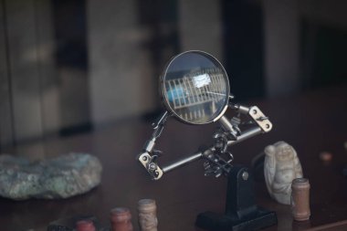 Modern bir bina cephesini yansıtan eklemli tutacağı olan bir büyüteç. Çeşitli antika eşyalar arasında bir mağaza vitrininde sergilendi. Optik, hassasiyet ve odaklanma için uygun