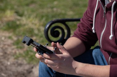 Yeşil bir parktaki bankta oturan uzaktan kumandalı bir drone 'u tutan birinin yakın çekimi. Teknoloji, açık hava aktivitesi ve modern eğlence için harika. Yüksek kalite fotoğraf