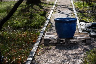 Peyzaj parkındaki ahşap palete yerleştirilmiş büyük boş bir seramik saksı. Bahçıvanlık blogları, tasarım modelleri ya da peyzaj ürünleri reklamları için uygun. Yüksek kalite fotoğraf