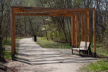 Modern ahşap kemerli, metal bisiklet parkı olan ve yeşil ağaçlarla çevrili bir park yeri. Kentsel manzara, kamusal alan tasarımı ve mimariyle ilgili görseller için ideal.