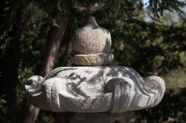 Yumuşak doğal ışık ve ağaç gölgeleriyle çevrili bir Japon bahçesinde oyulmuş detaylarla dolu geleneksel bir taş fenerin yakın çekimi. Doğa, bahçe ve mimari temalar için ideal. Kullanılabilir.