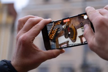 Akıllı telefonu olan bir adam, Wroclaw, Polonya 'nın merkezindeki şenlikli Noel pazarının videosunu çekiyor. Arka plan süslemeler, çelenkler ve aydınlık pazar tezgahlarıyla dolu. Festival etkinlikleri ve şehir tatili temaları için ideal