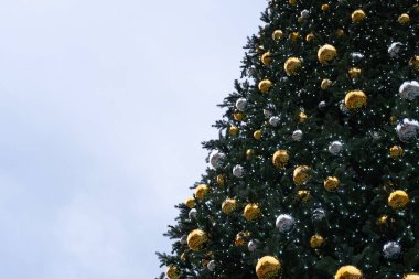 Açık mavi gökyüzüne konan altın ve gümüş süslemelerle süslenmiş bir Noel ağacının yakın çekimi. Bu resim tebrik kartları, tatil posterleri ve yeni yıl gelenekleri için idealdir.