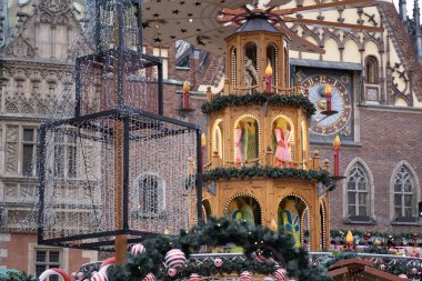 Polonya 'nın Wroclaw şehrinde bir Noel piyasa sahnesi. Resim, heykelcikler, mumlar ve çelenklerle süslenmiş güzel dekore edilmiş ahşap bir piramidi içeriyor. Arka planda tarihi Avrupa mimarisi ve saat kulesi var.