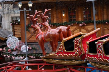 Polonya 'nın Wroclaw şehrinde bir Noel atlıkarıncasında ren geyiğiyle renkli kırmızı kızaklara yakın durun. Arka planda süslü Noel market tezgahları, ışıklar ve şenlikli bir atmosfer yer alıyor. Kış tatillerini ve Noel 'i resmetmek için mükemmel. 