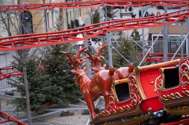 Polonya 'nın Wroclaw kentindeki bir atlıkarıncaya yerleştirilmiş ren geyikli Noel kızakları manzarası. Arka planda yeşil Noel ağaçları ve şenlikli ışıklar görünüyor. Sihirli bir kış havası yaratıyor. Kış fuarları, tatil süslemeleri ve Chris için ideal.