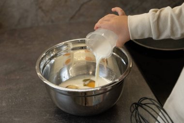 Küçük bir el ölçü kabını tutar ve krep hamuruna süt döker. O, çok rahat bir mutfakta karanlık yumuşak tonlarda bastırılmış ışıklandırmayla yemek pişiriyor. Ailesinin mutfağında iyi bir yardımcı. Fotoğraf indepe gelişen bir eğitim sistemini yansıtıyor