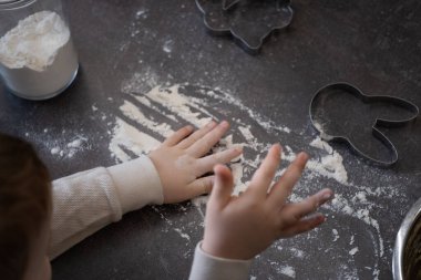 Koyu bir tezgahta un keşfeden bir çocuğun elleri, tavşan şeklinde kurabiye kesicilerle çevrili. Paskalya pişirme temaları, duyusal oyun içeriği ve blog, reklam veya eğitim için aile odaklı görseller için ideal.