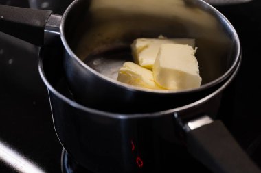 Kaynar suyun üzerine yerleştirilmiş küçük bir tencerede eriyen tereyağı parçaları çifte kazanlı bir yöntem gösteriyor. Bu detaylı mutfak sahnesi temel yemek pişirme adımlarını, tarif talimatlarını göstermek için idealdir.