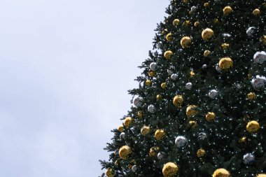 Açık mavi gökyüzüne konan altın ve gümüş süslemelerle süslenmiş bir Noel ağacının yakın çekimi. Bu resim tebrik kartları, tatil posterleri ve yeni yıl gelenekleri için idealdir.