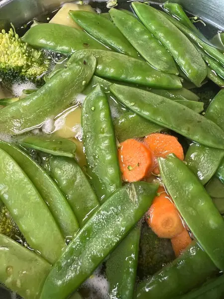 Suya batırılmış taze bezelye, havuç ve brokoli, doğal dokuları ve canlı renkleri ön plana çıkarıyor. Sağlıklı yemek pişirme, bitki temelli diyet, vegan tarifler veya organik yaşam tarzı içeriği konuları için idealdir. Aşçılık blogunda kullanılabilir