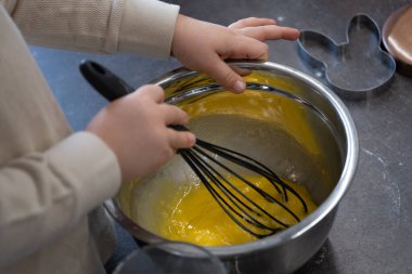 Metal bir kasede yumurta ve şeker karışımı karıştıran bir çocuğun en iyi görüntüsü. Childs 'ın elleri çırpıcıyı sıkıca tutuyor, yemek pişirme sürecine odaklandığını gösteriyor. Mutfaktaki çocuk aktivitelerini, aile tariflerini ya da eğitimsel aktiviteleri göstermek için mükemmel. 