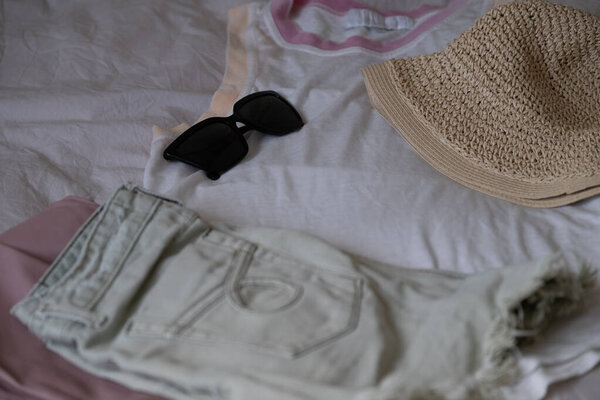 Платье повседневной летней одежды, включая легкие джинсовые шорты, белый топ танка с розовой отделкой, черные солнцезащитные очки и соломенную шляпу. Перфект для статей в блогах, социальных сетей, планирования отпуска и продвижения модной одежды.