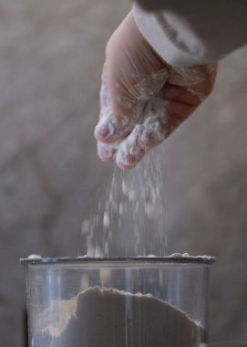 Küçük bir çocuk mutfakta yardım ederken şeffaf bir kabın içine un serpiyor. Bu yakın çekim, evde pişirme etkinliği sırasında duyusal olarak zengin bir anı yakalıyor. Aile yemeklerini, çocuk gelişimini veya eğitici gıda içeriğini resmetmek için ideal