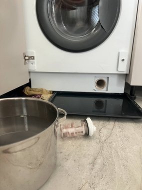 Çamaşır makinesinin filtresinin temizleme işlemini gösteren gerçek bir fotoğraf. Süzgeç, su kovası ve havlu çıkarılmış. Ev bakımını, alet bakımını, tesisat sorunlarını ya da DIY tamir derslerini göstermek için kullanışlı. Bloglar için uygun, 