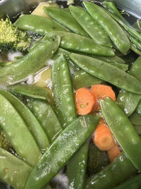 Suya batırılmış taze bezelye, havuç ve brokoli, doğal dokuları ve canlı renkleri ön plana çıkarıyor. Sağlıklı yemek pişirme, bitki temelli diyet, vegan yemek tarifleri ya da