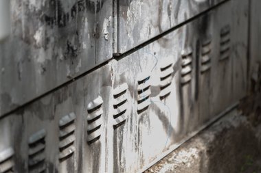 Çoklu havalandırma delikleri, görünür çizikler, lekeler ve kabloların bulunduğu yıpranmış metal bir duvarın yakın çekimi. Tasarım projelerinde arka planlar, kentsel bozulma kavramları, grunge dokuları veya teknik altyapı temaları için ideal.