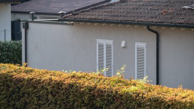 Basit bir banliyö evi, beyaz pencere panjurları ve eğimli kiremitli çatısı, kısmen kırpılmış bir çitin arkasına gizlenmiş. Sahne huzurlu ve temiz. Ev kavramlarını resmetmek için ideal.