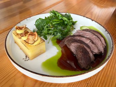 Zengin soslu orta pişmiş sığır eti, çıtır garnitür katmanlı patates ızgarası ve taze yeşil salata içeren zarif bir restoran tabağı. Güzel yemek ve gurme mutfağını resmetmek için ideal.