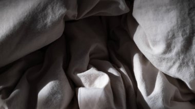 Doğal ışıkla aydınlatılan kırışık beyaz kumaşın yakın çekim görüntüsü samimi ve dokunsal bir doku yaratıyor. Yumuşak kıvrımlar ve gölgeler pamuk maddesinin organik yapısını vurgular. Bu minimalist arkaplan iç tasarım ve tekstil için idealdir. 