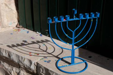 A blue, metal Hanukkah menora casts a shadow on a stone wall outside a Jerusalem home in the daytime during the Festival of Lights in Israel.  clipart