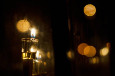 The shamash, or additional helper candle on the menorah, glows brightly in this artistic image of oil Hanukkah candles burning in a glass housing during the celebration of the Festival of Lights in Israel.  clipart