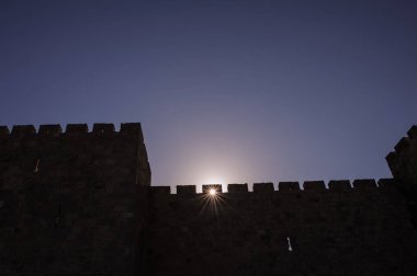 A section of the ancient stone ramparts and walls of the Old City of Jerusalem, in silhouette with a sunstar at sunrise on Mt. Zion.  clipart