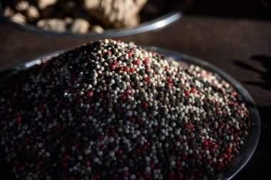 Large silver bowl filled with fresh, whole red, black and white peppercorns piled high and bathed in sunlight. 