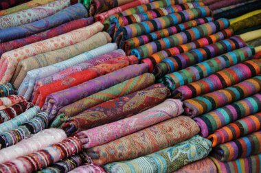 Closeup detail of piles of colorful, patterned cashmere pashmina scarves being sold in a Middle Eastern market. .  clipart