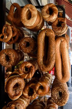 Variety of freshly baked, seeded bagels and round breads hang on a metal rack in a Tel Aviv, Israel bakery.  clipart