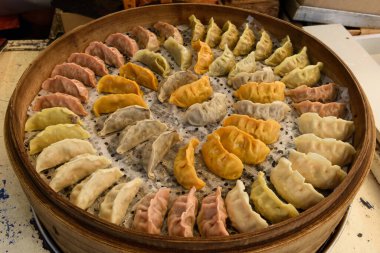 Variety of steamed vegetable dumplings made from tomato, sweet potato and white flour doughs arranged in a decorative, circular pattern on a round, bamboo tray.  clipart