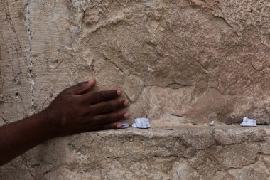 Bir adam elini, Kudüs 'te dua ederken Batı Duvarı' nın pürüzsüz desenli taşlarına bastırır..