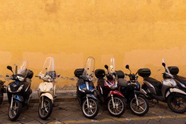 Floransa, İtalya 'da bir kaldırımda, parlak sarı bir duvarın önüne park edilmiş birden fazla scooter var.. 