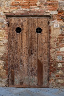 Lucignano, Tuscany, İtalya 'daki eski, ahşap, boyanmamış ve bozulmakta olan kırmızı tuğlalı bir binanın temelinde iki adet yuvarlak kapısı olan bir kapı.. 