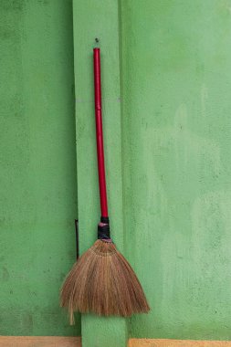 A simple, straw broom with red, wooden handle hanging neatly on a green wall outside a home in rural northern Vietnam. 