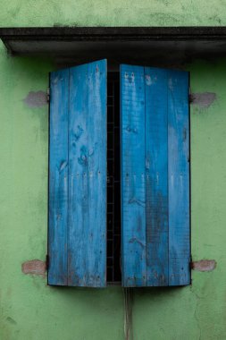 Bir çift solmuş, yontulmuş, boyanmış, hafif açık mavi ahşap panjurlar, Kuzey Vietnam 'ın kırsal kesimindeki bir evde yeşil bir duvara karşı.. 