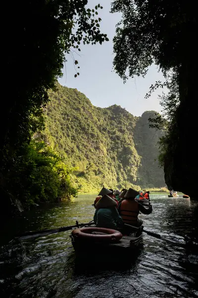 Turistlerle dolu küçük kayıklar, Tam Coc, Ninh Binh vilayeti, Kuzey Vietnam 'daki kireçtaşı dağlarının ortasındaki bir nehirdeki mağaradan çıkıyor.. 