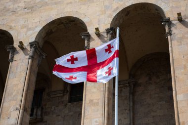 Gürcistan Cumhuriyeti bayrağının beyaz arka planında kırmızı haçlar, Tiflis 'te rüzgarda savrulan bir bayrak direğinin tepesinde..