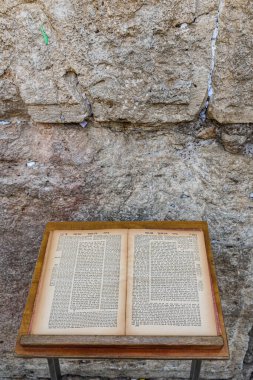 An aged volume of the Jewish Talmud open to a page of text from chapter eight of the tractate Bava Kama rests on a prayer stand in front of the Western Wall in Jerusalem.	