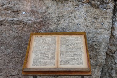 An aged volume of the Jewish Talmud open to a page of text from chapter eight of the tractate Bava Kama rests on a prayer stand in front of the Western Wall in Jerusalem.	
